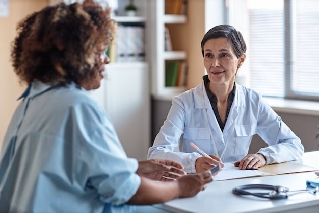 Friendly Female Obstetrician Talking to Patient A female doctor in a white coat smiles while talking to a patient across a desk in a medical office.