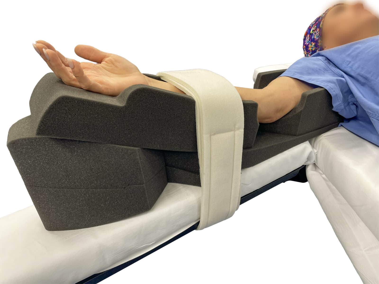 EEC Patient Supine 6 - edit A person lies on a hospital bed with their arm resting in a black foam positioning device, likely for stabilization, while wearing a smartwatch. Medical equipment is visible in the background.